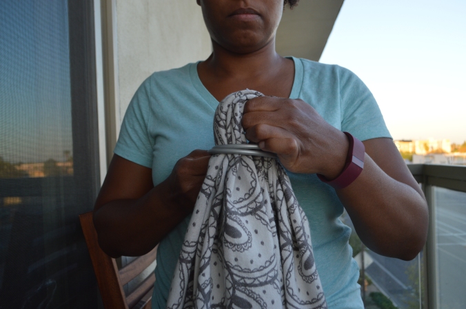 Image shows the brown skin woman feeding the looped wrap through both of the large silver aluminum sling rings